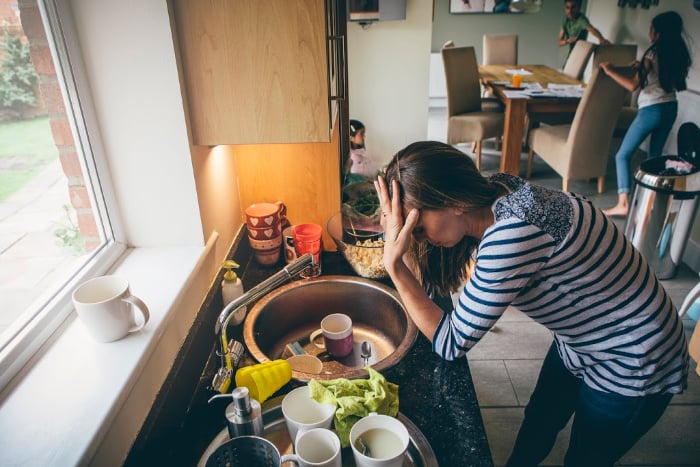 woman at sink feeling bad with dishes everywhere and children in the background