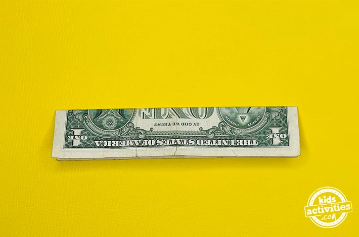 Bouteille en origami pour billets d'un dollar - Étape 1 - Pliez le billet en deux sur la largeur.  Tutoriel du blog d'activités pour enfants