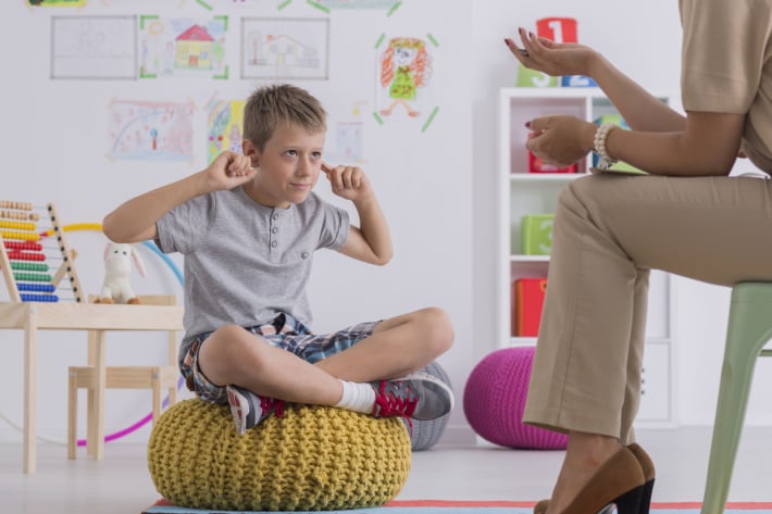 child sitting on a bean bag in front of a teacher with fingers in ears not listening at age 8