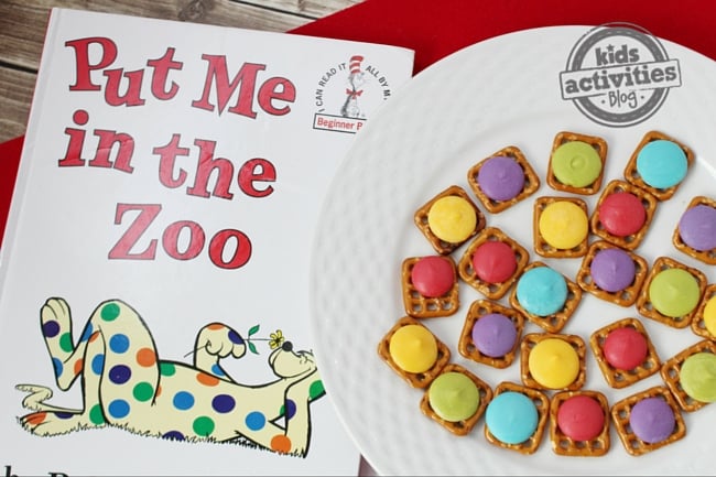 Livre Put Me In The Zoo et artisanat comestible - des carrés de bretzel avec des bonbons bleu violet rouge vert et jaune fondent sur une assiette blanche sur un fond rouge et bois - blog d'activités pour enfants