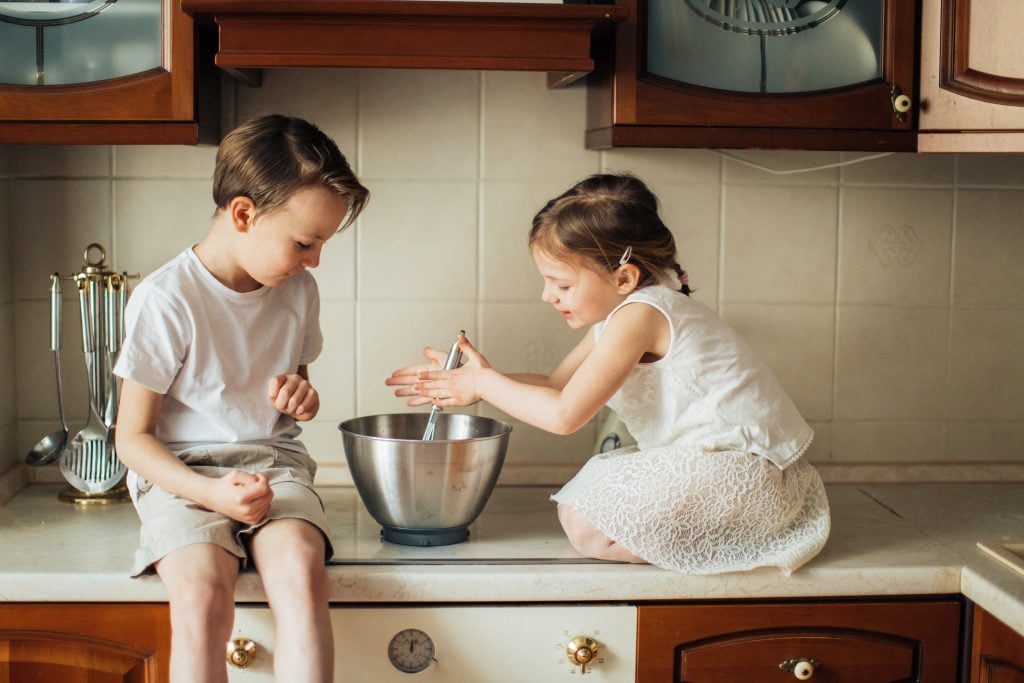Apprenez à lire une recette et à cuisiner, une petite fille et un garçon sur un comptoir fouettant dans un bol en acier - Compétences de vie à l'ancienne