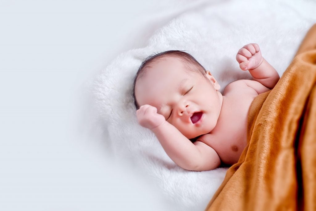 Prénoms de bébé des années 1990 : bébé dormant tranquillement dans un berceau recouvert d'une couverture colorée