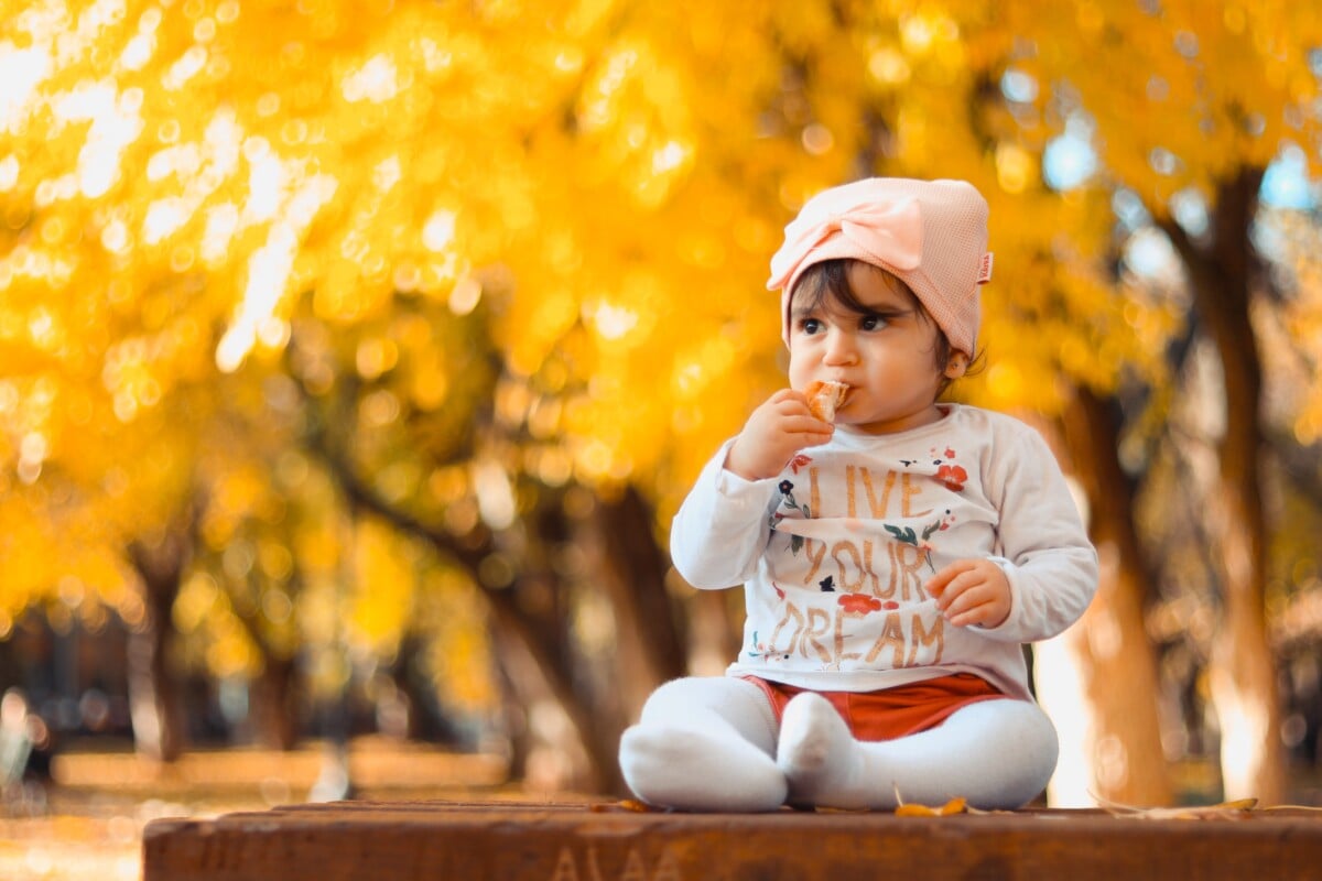Noms de bébé des années 90 - Petite fille assise sur une table avec des arbres d'automne autour d'elle