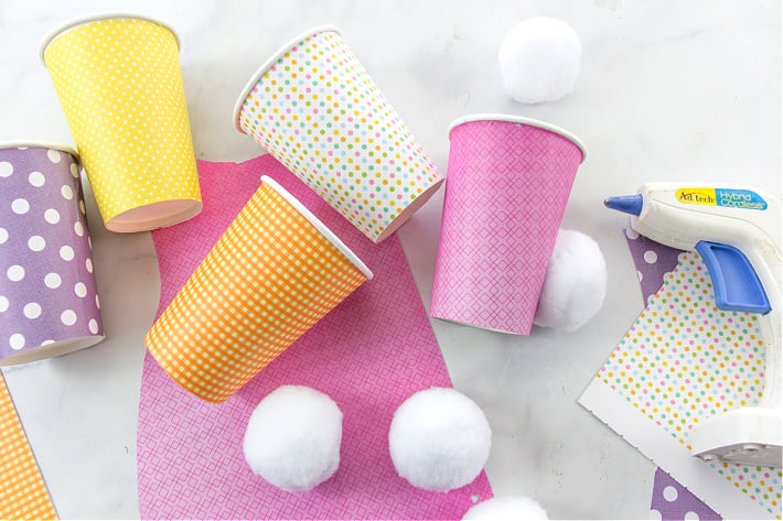 L'étape 2 pour fabriquer des gobelets à mélange de collations avec des fesses de lapin consiste à attacher des pompons aux gobelets à l'aide de colle chaude.