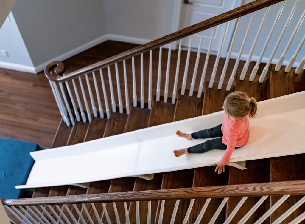 Glissière d'escalier illustrée sur un escalier en bois avec un enfant glissant au milieu de l'escalier