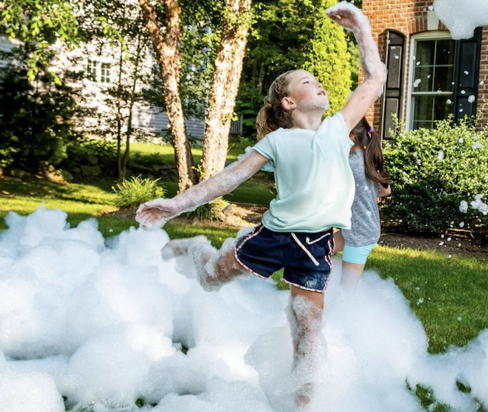 Fille dansant à travers les bulles et la mousse fabriquées par le fabricant de bulles Fom Mania Fomalanche à l'extérieur