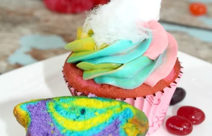 cupcake rouge avec un glaçage arc-en-ciel sur le dessus - garni de barbe à papa blanche
