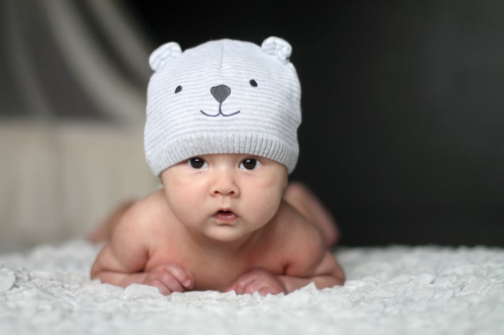 bébé sur le ventre regardant la caméra avec des yeux marron portant un chapeau d'ours