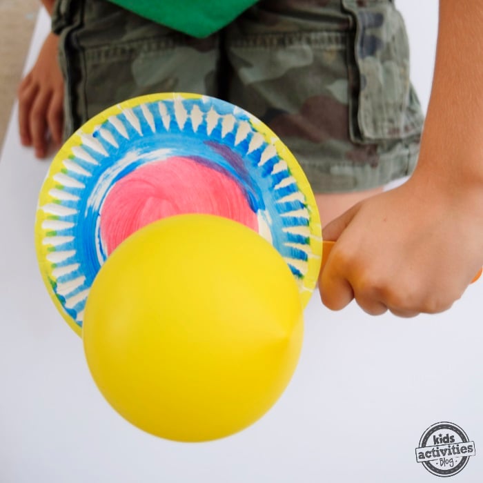 Jeu de tennis en assiettes en papier - un garçon utilise une pagaie de tennis en assiettes en papier pour frapper un ballon jaune - blog d'activités pour enfants