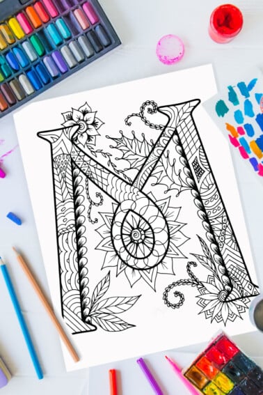 Pages à colorier de l'alphabet Zentangle - lettre m design zentangle sur fond de peinture, crayons de couleur et fournitures d'art