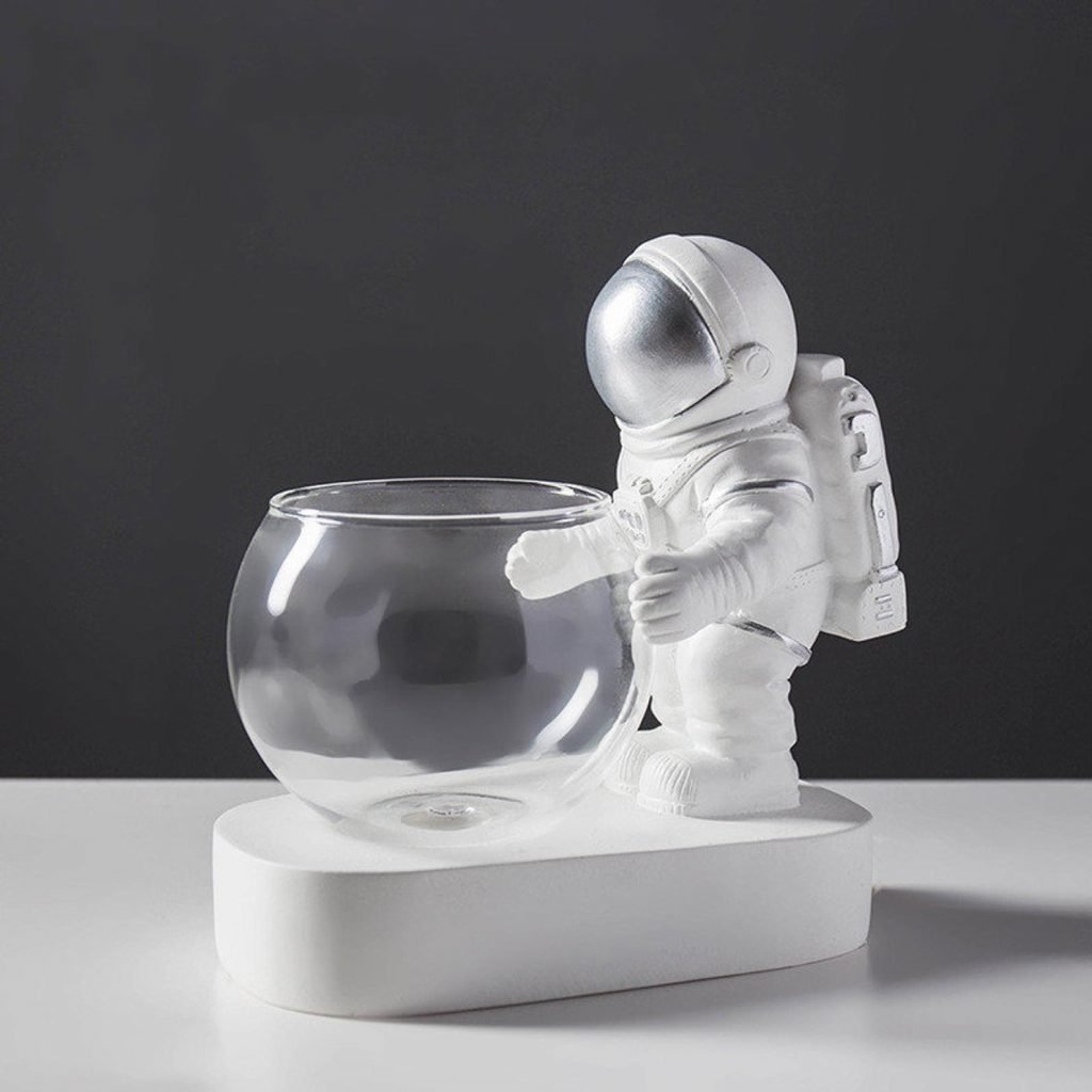 Astronaute argenté tenant un vase transparent prêt à être planté sur un fond noir et blanc