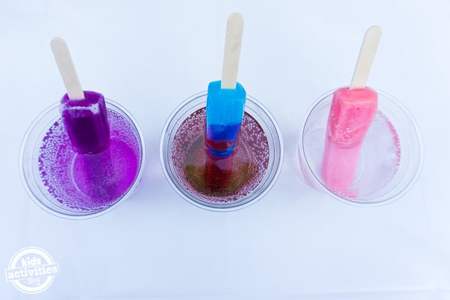 3 sucettes glacées (raisin, bleu et rose) chacune dans un verre à soda transparent sur le dessus avec les couleurs de la glace s'infiltrant dans le soda