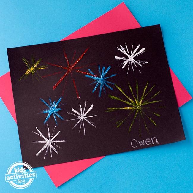 Artisanat de feux d'artifice fini - papier noir avec feux d'artifice de peinture rouge, jaune, blanc et bleu avec des paillettes sur fond bleu et rose - blog d'activités pour enfants