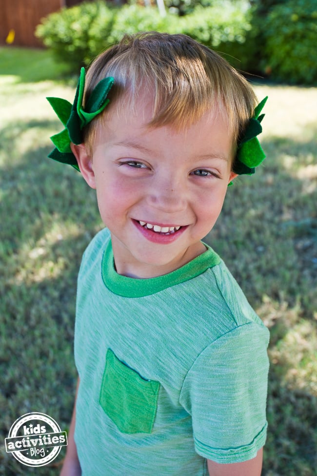 Couronne de feuilles de laurier à faire soi-même - Terminé - Petit garçon souriant dans une chemise verte portant une couronne de feuilles à l'extérieur - Blog d'activités pour enfants