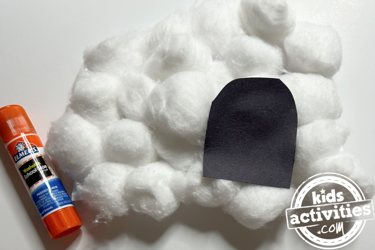 Étape 3 - Bricolage avec une assiette en papier Igloo - Découpez une petite forme de porte avec le papier de construction noir et collez-la dessus. - Blog d'activités pour enfants