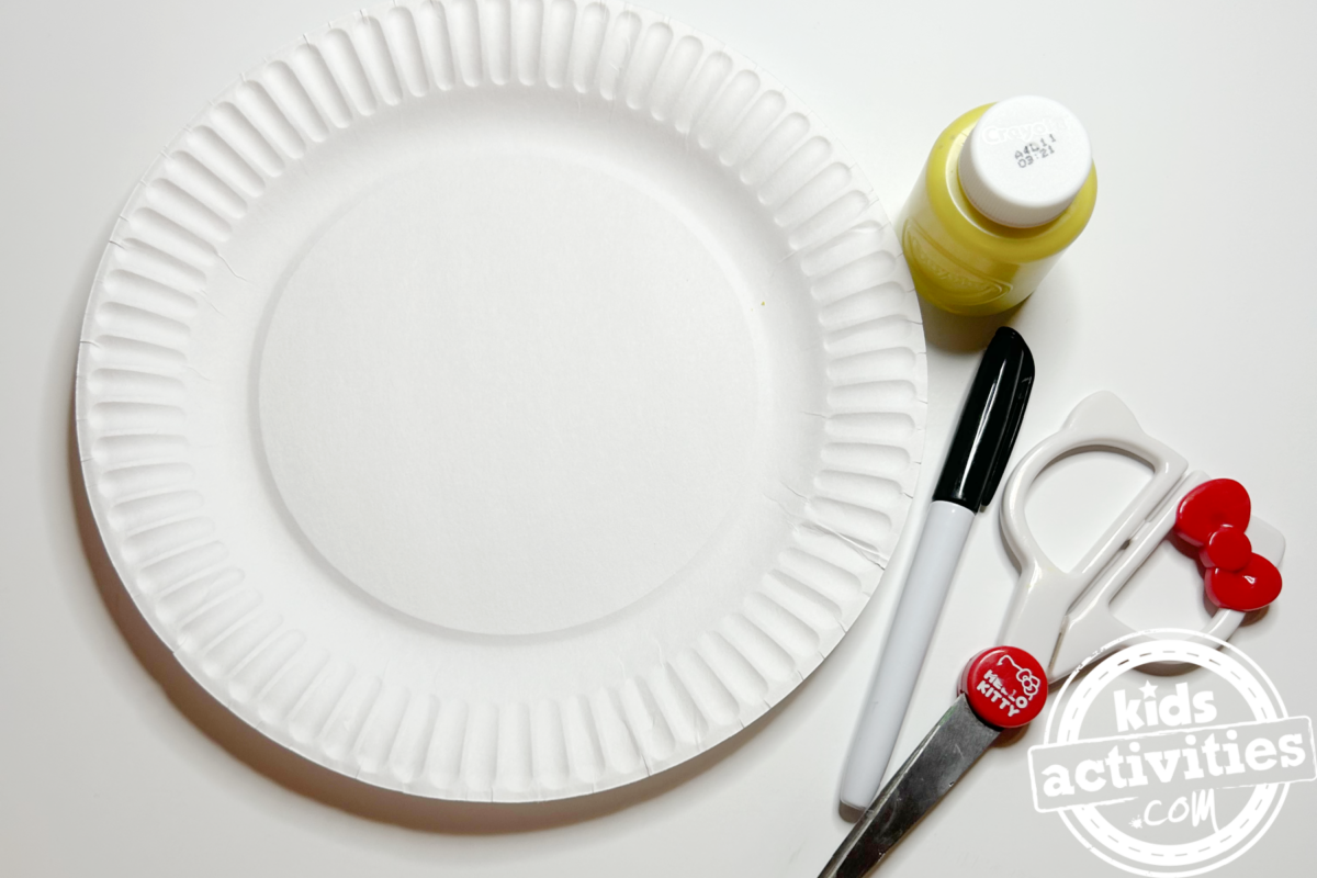 Fournitures nécessaires pour fabriquer une assiette en papier en forme de lune : une assiette en carton, de la peinture jaune, un feutre, des ciseaux et un pinceau - Blog d'activités pour enfants