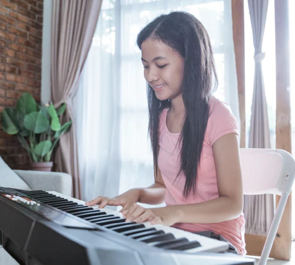 L'image montre une collégienne jouant du piano électrique à l'intérieur d'une maison.
