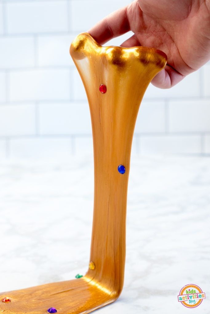 Slime Infinity Gauntlet fait maison étiré à la main sur un fond blanc - slime doré avec des pierres précieuses rouges, bleues, violettes, jaunes et vertes.