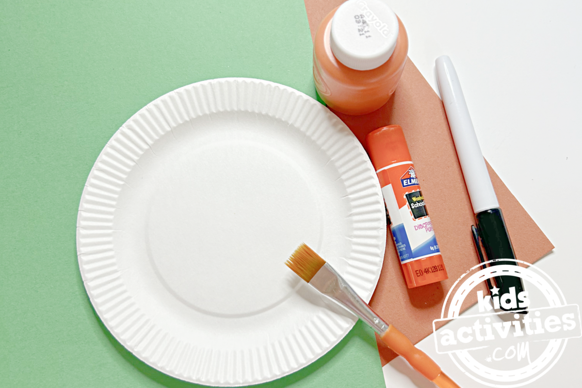 Fournitures nécessaires pour fabriquer une assiette en carton orange : du papier de construction marron et vert, de la peinture orange, une assiette en carton, des ciseaux, un feutre et un pinceau - Blog d'activités pour enfants