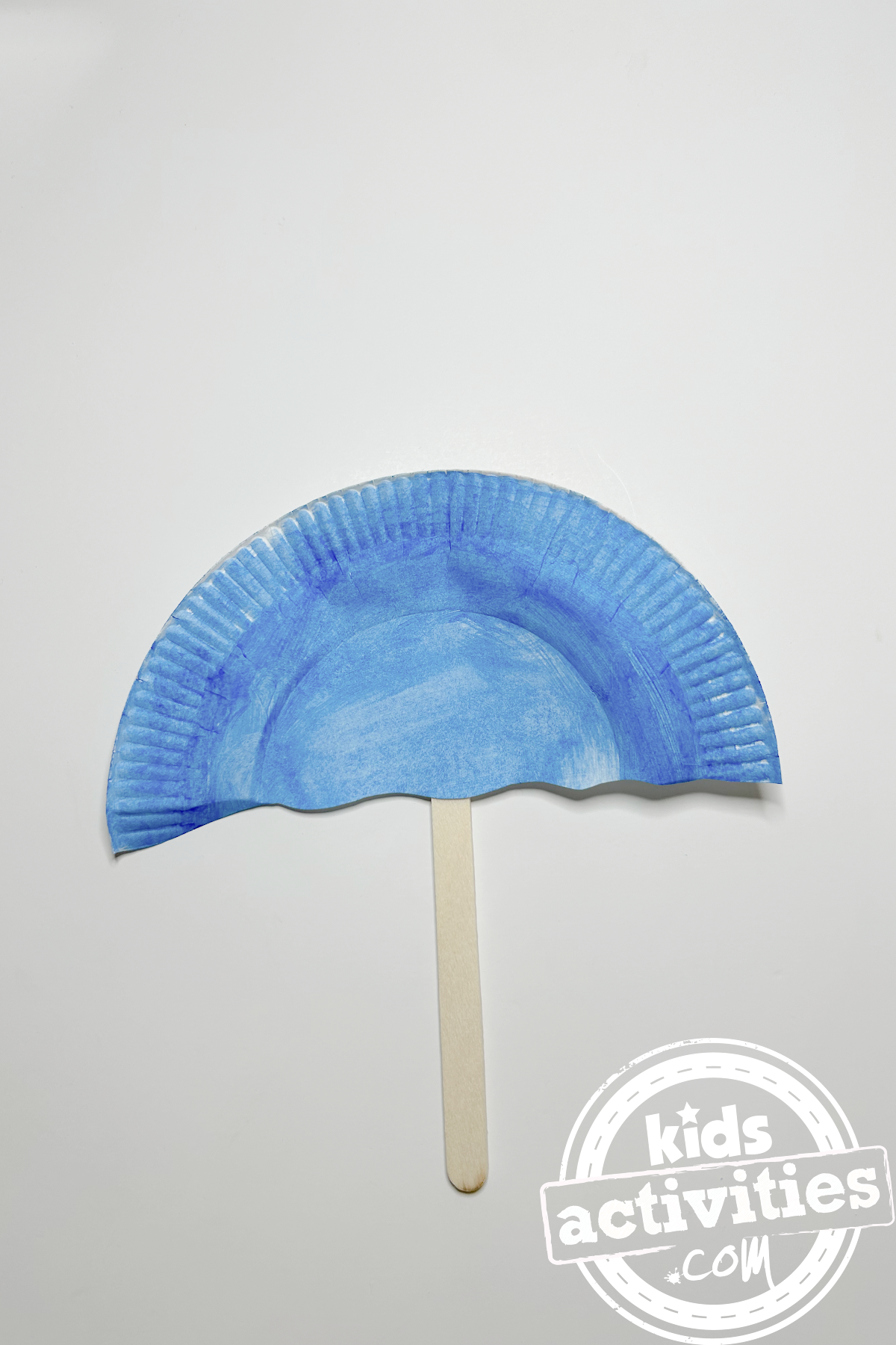 Bricolage en assiette en carton avec parapluie sur fond blanc avec un dessus de parapluie bleu et un dessous de bâtonnet de glace - blog d'activités pour enfants