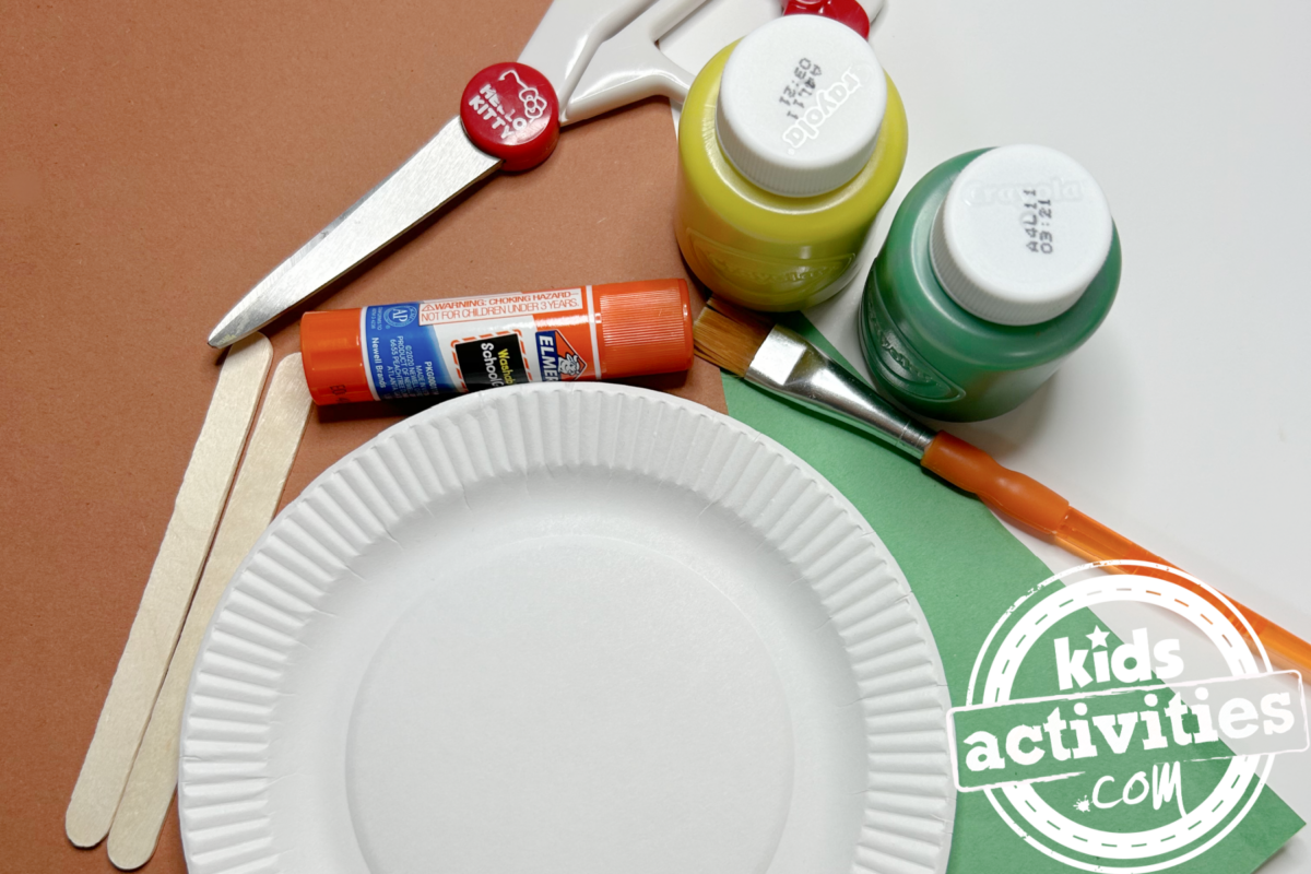 Fournitures nécessaires pour fabriquer une assiette en papier tournesol : du papier de construction marron et vert, une mini assiette en papier, deux bâtonnets de glace, de la peinture jaune et verte, de la colle, des ciseaux et un pinceau - blog d'activités pour enfants