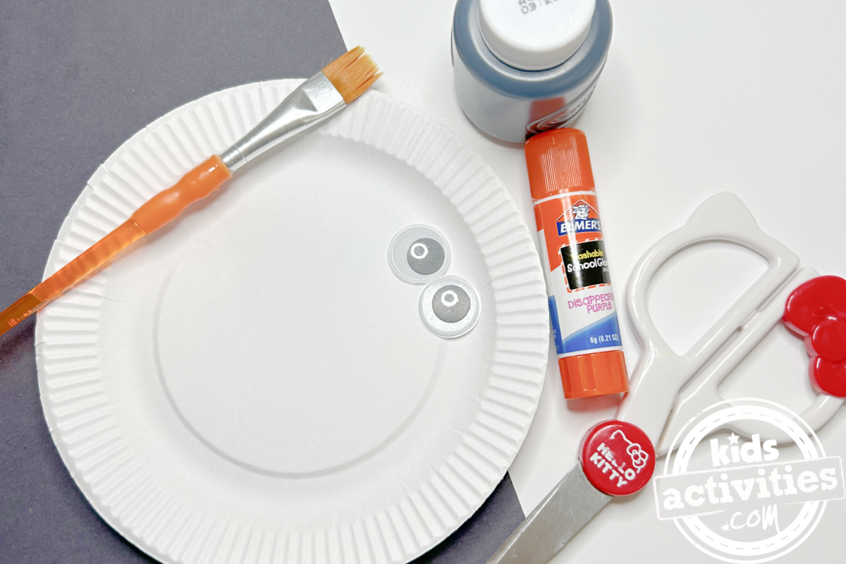 Fournitures nécessaires pour fabriquer un raton laveur en assiette en carton : du papier de construction noir, une mini assiette en carton, de la peinture grise, de la colle, des yeux mobiles, des ciseaux et un pinceau - Blog d'activités pour enfants