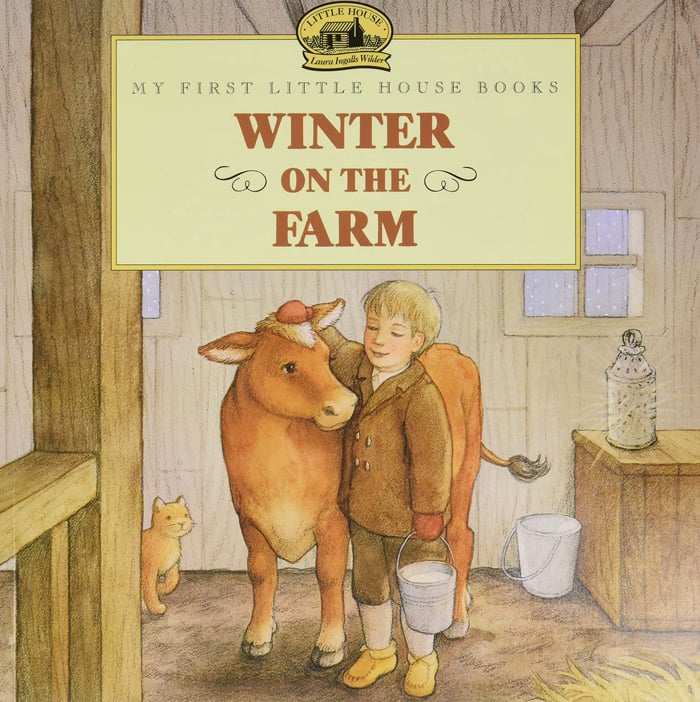 histoire d'animaux pour les enfants - L'image montre un jeune garçon vêtu de marron grattant la tête d'une vache brune dans une stalle de grange tout en tenant un seau en argent rempli de lait frais avec un chat orange assis en arrière-plan d'Amazon.