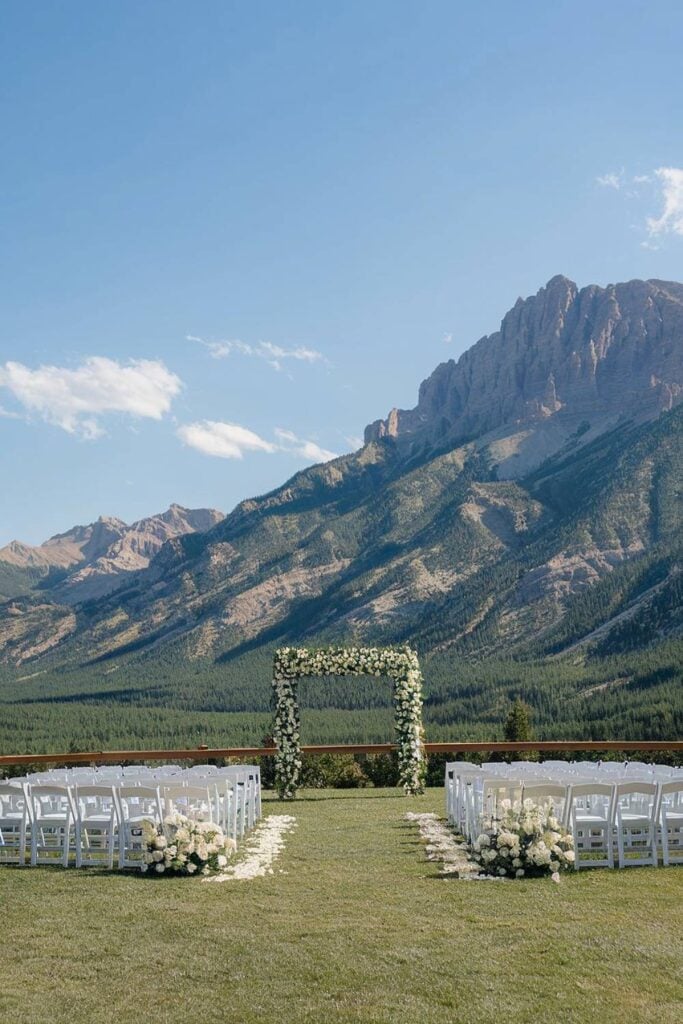 Mariage en montagne avec arche fleurie et chaises blanches.