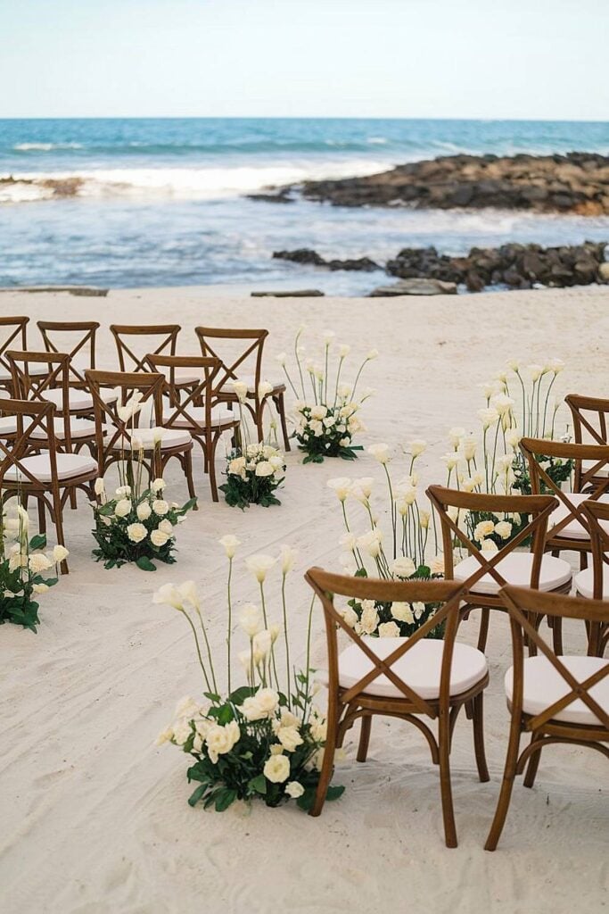 Configuration de mariage sur la plage avec chaises en bois et fleurs blanches au bord de l'océan.