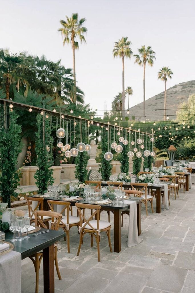Configuration de mariage dans le jardin avec de la verdure et des globes lumineux suspendus pour un micro-mariage.
