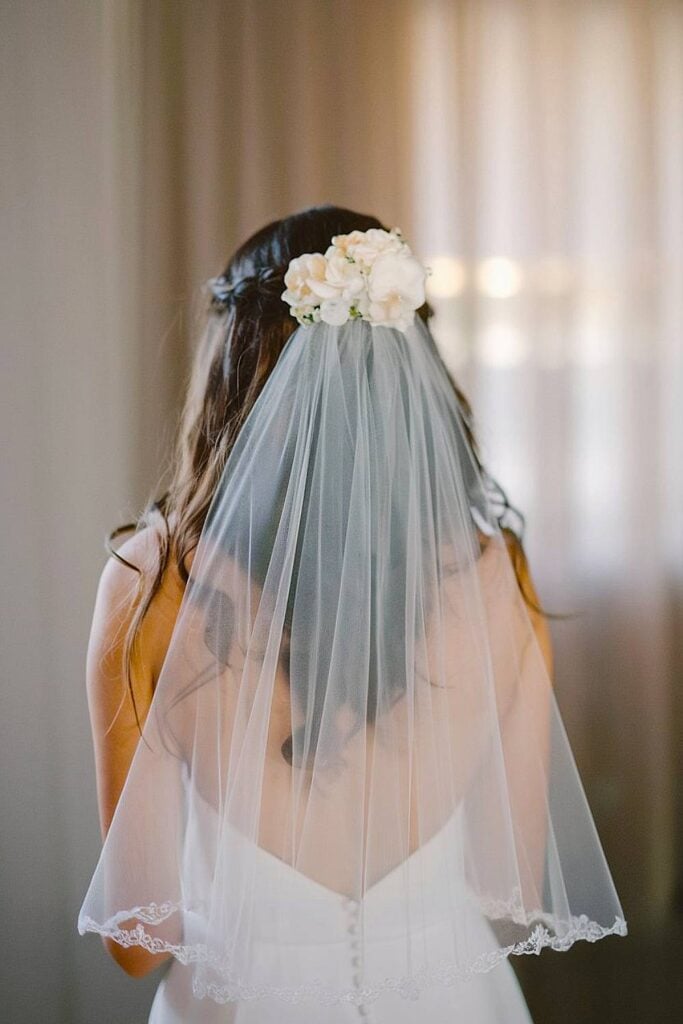 Mariée avec voile bordé de dentelle et accent floral pour micro-mariage.