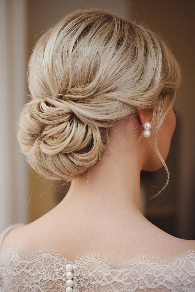 Chignon de mariage de luxe sophistiqué avec chignon doux et boucles d'oreilles en perles.
