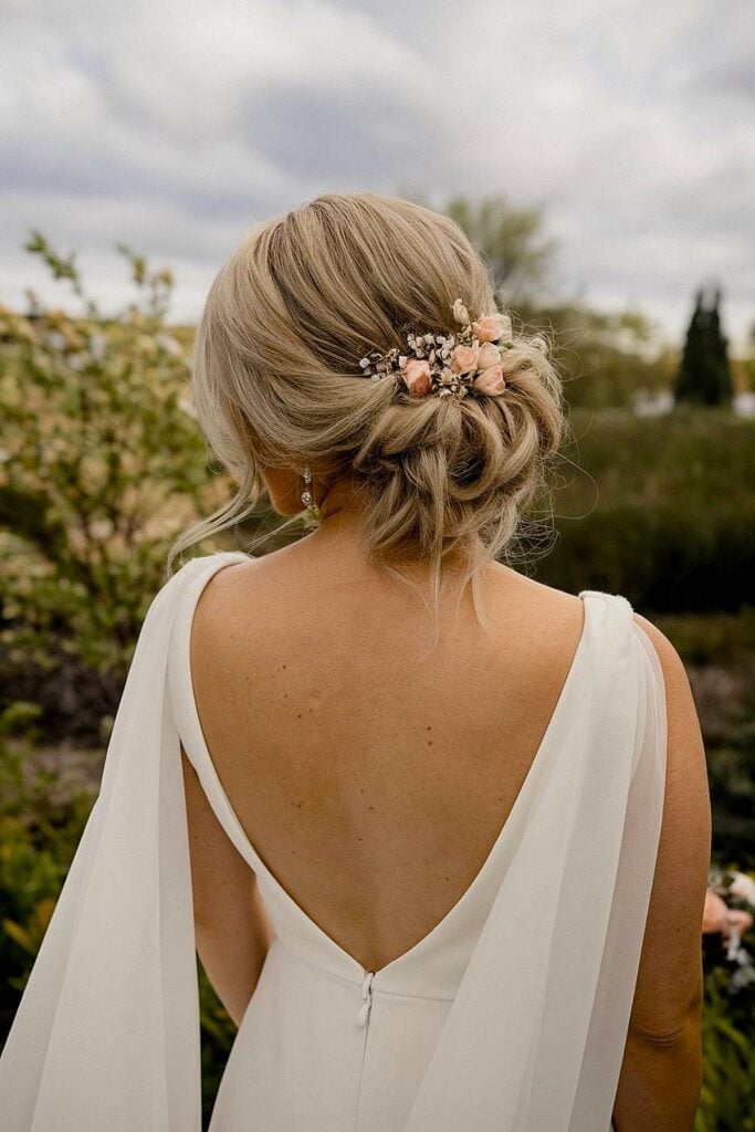 Chignon ample de la mariée avec des fleurs roses pour un mariage dans la cour.