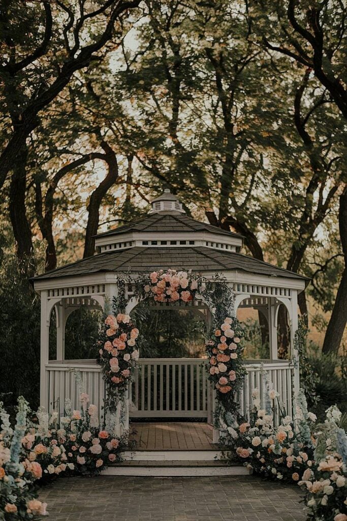 Gazebo décoré de roses blush et de verdure pour un mariage dans la cour.