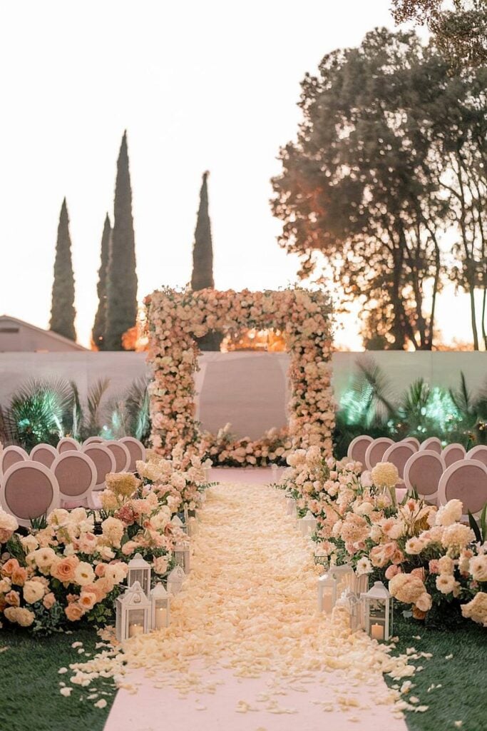 Allée de pétales de rose avec décor floral blush pour un mariage dans la cour.