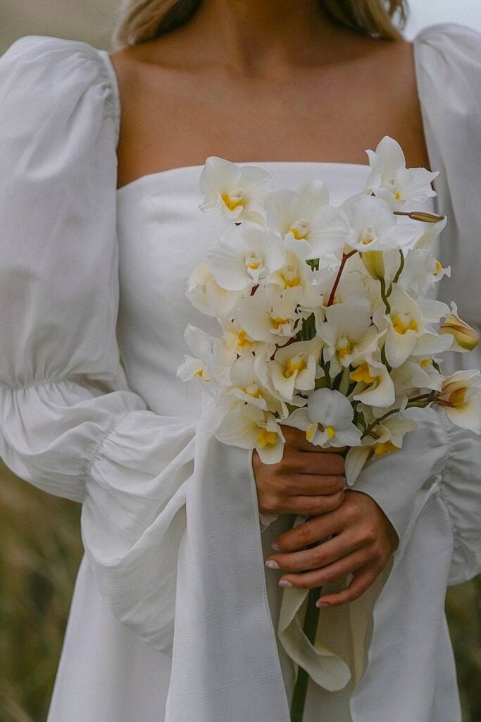 Mariée tenant un bouquet d'orchidées blanches pour un mariage dans la cour.