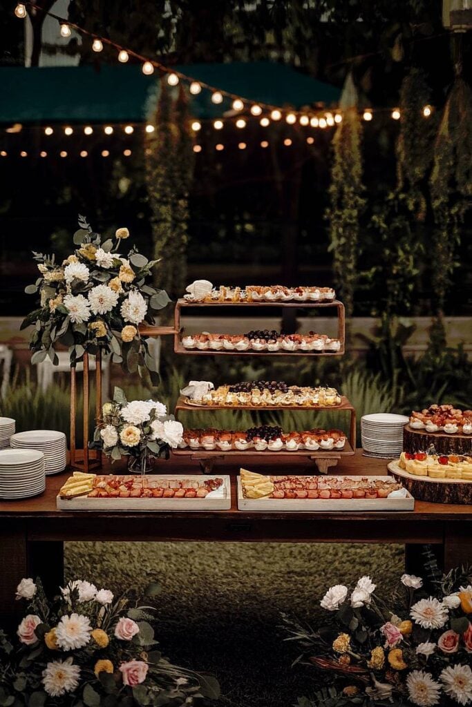 Table d'apéritifs et de desserts à plusieurs niveaux avec fleurs pour un mariage dans la cour.