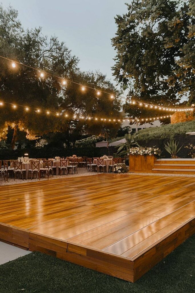 Piste de danse de mariage en bois avec guirlandes lumineuses.