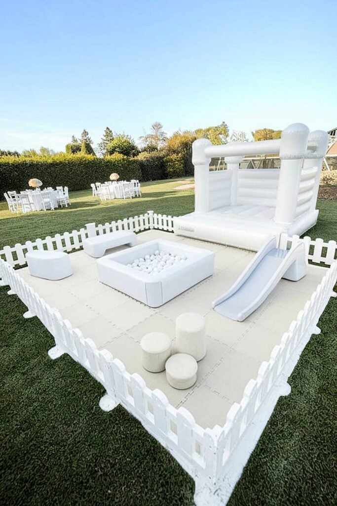 Aire d'activités pour enfants entièrement blanche avec maison gonflable pour mariage dans la cour.
